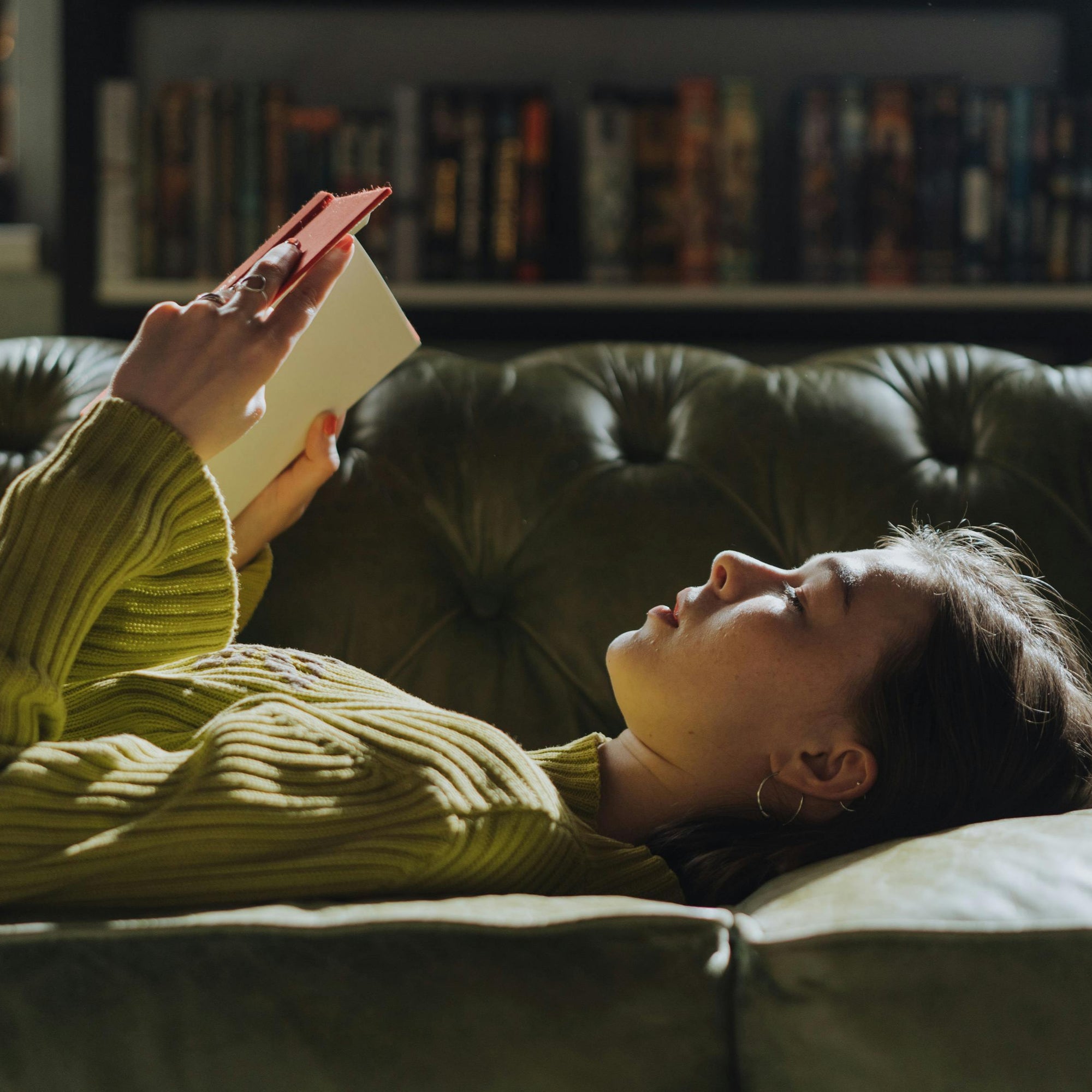 Woman lying on a couch reading a book in a cozy living room.